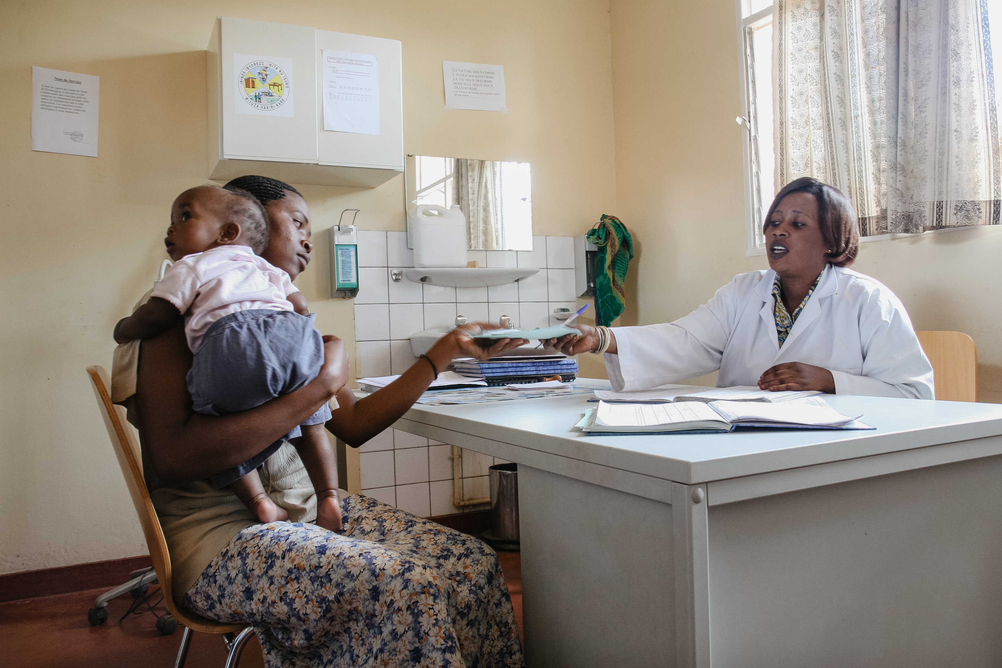 A clinician consults with a mother holding her child in a clinic.