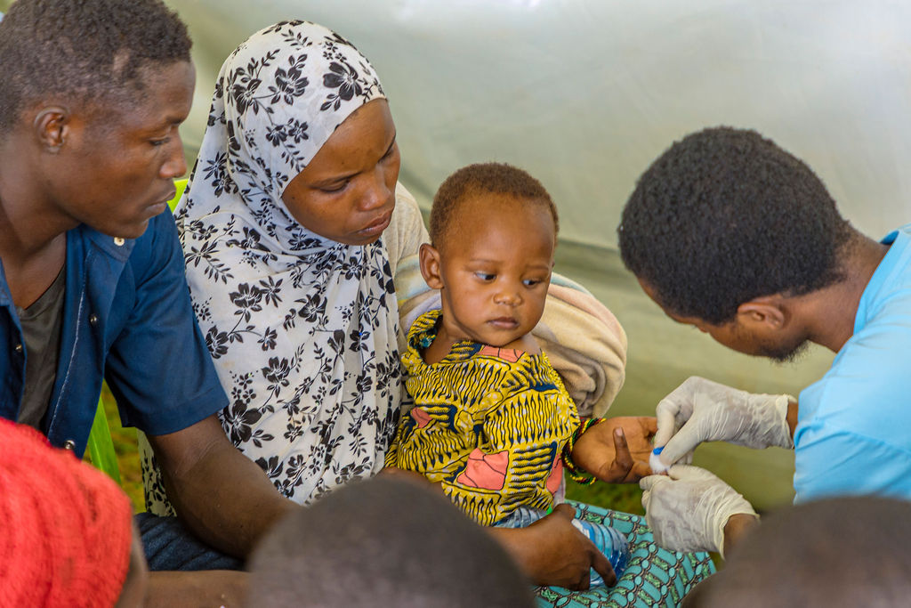 A health worker screens a young child while the family looks on.